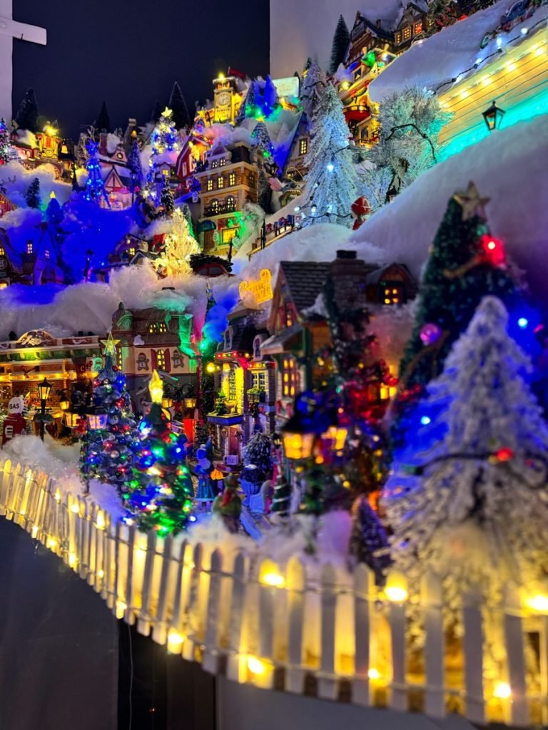 Perspective du village de Noël avec une barrière lumineuse et des maisons installées en hauteur.