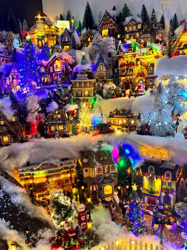 Vue d’ensemble du village de Noël illuminé avec ses maisons, ses arbres et ses scènes enneigées.